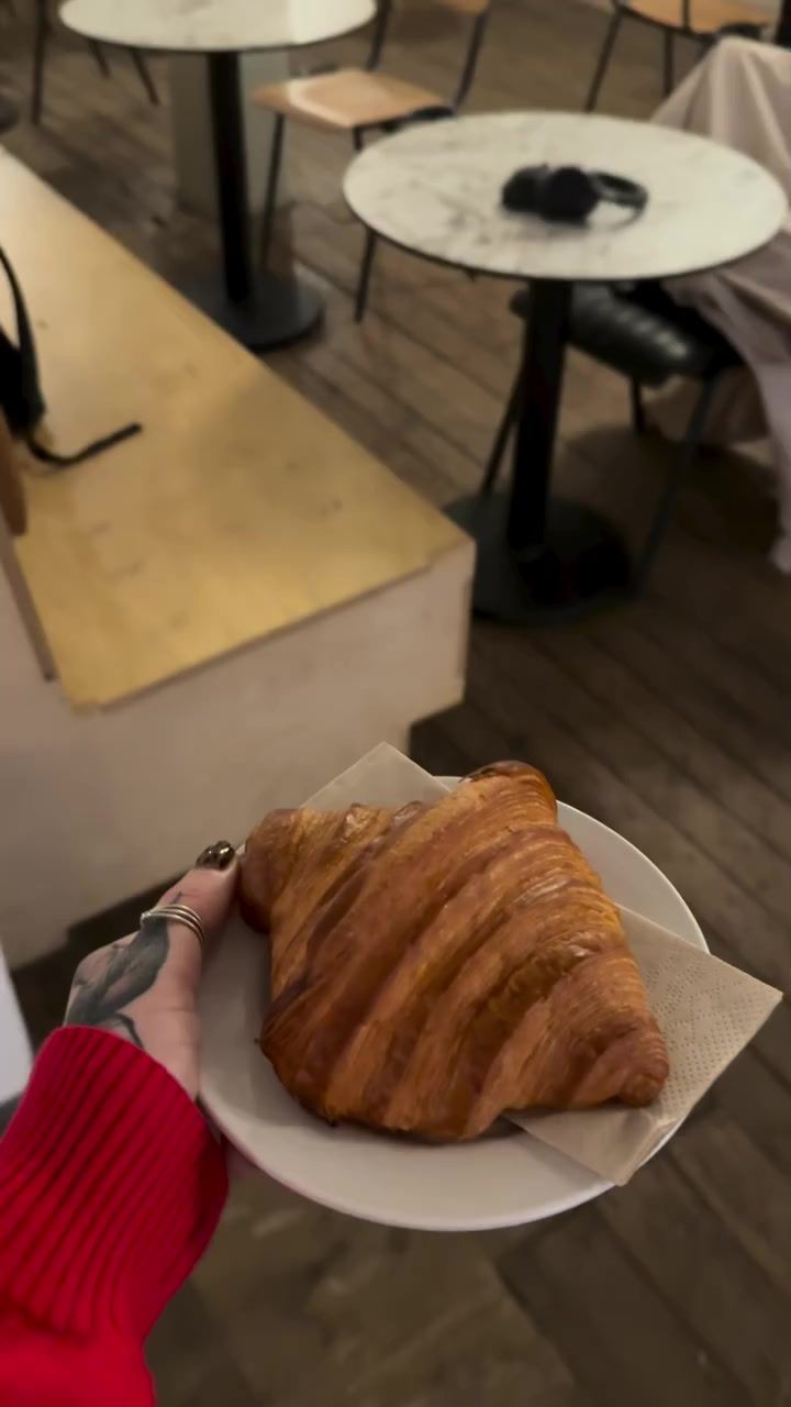A croissant on a plate, held up in a red sleeve