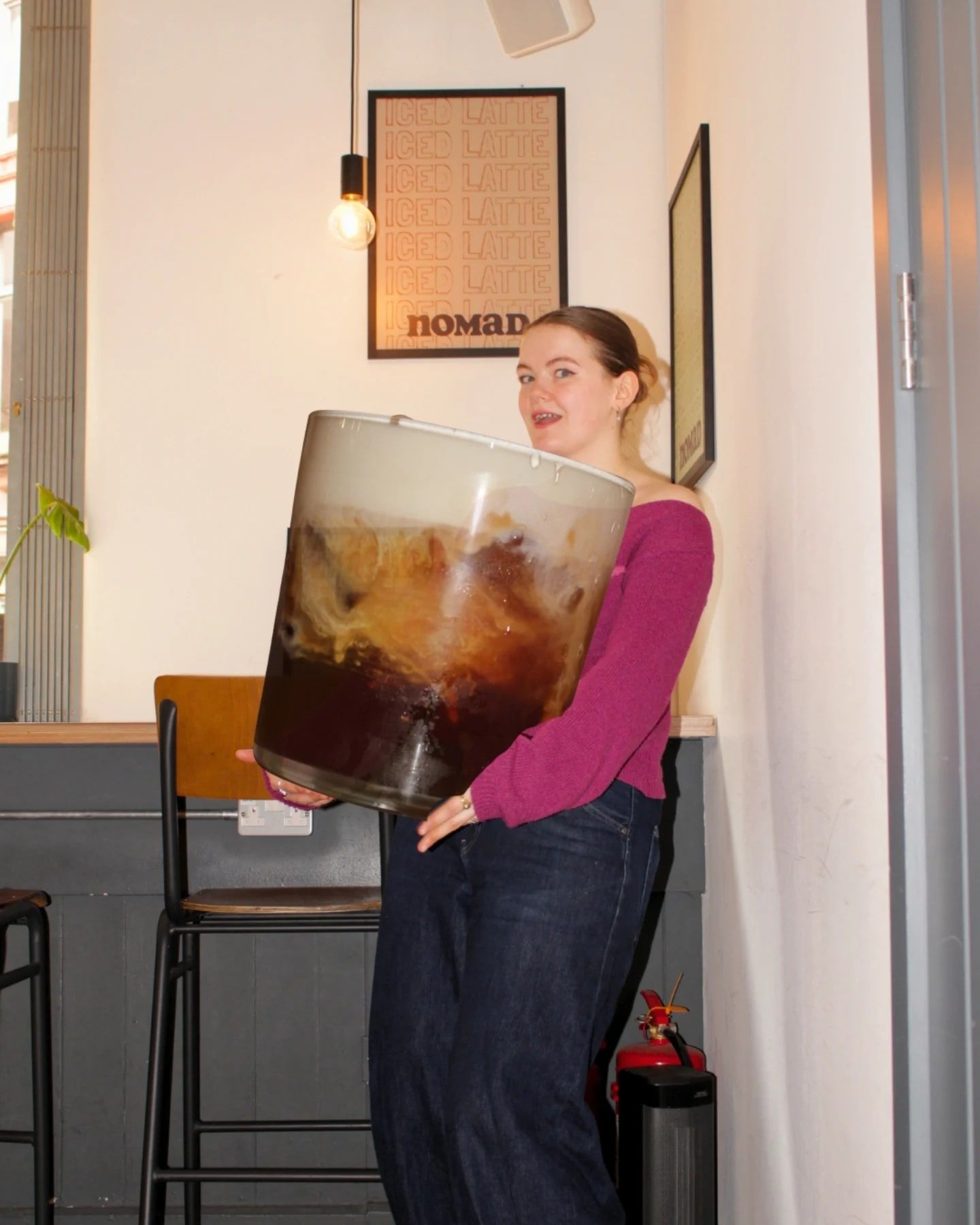 Hugging a giant iced coffee in a nomad cup, almost as big as she is
