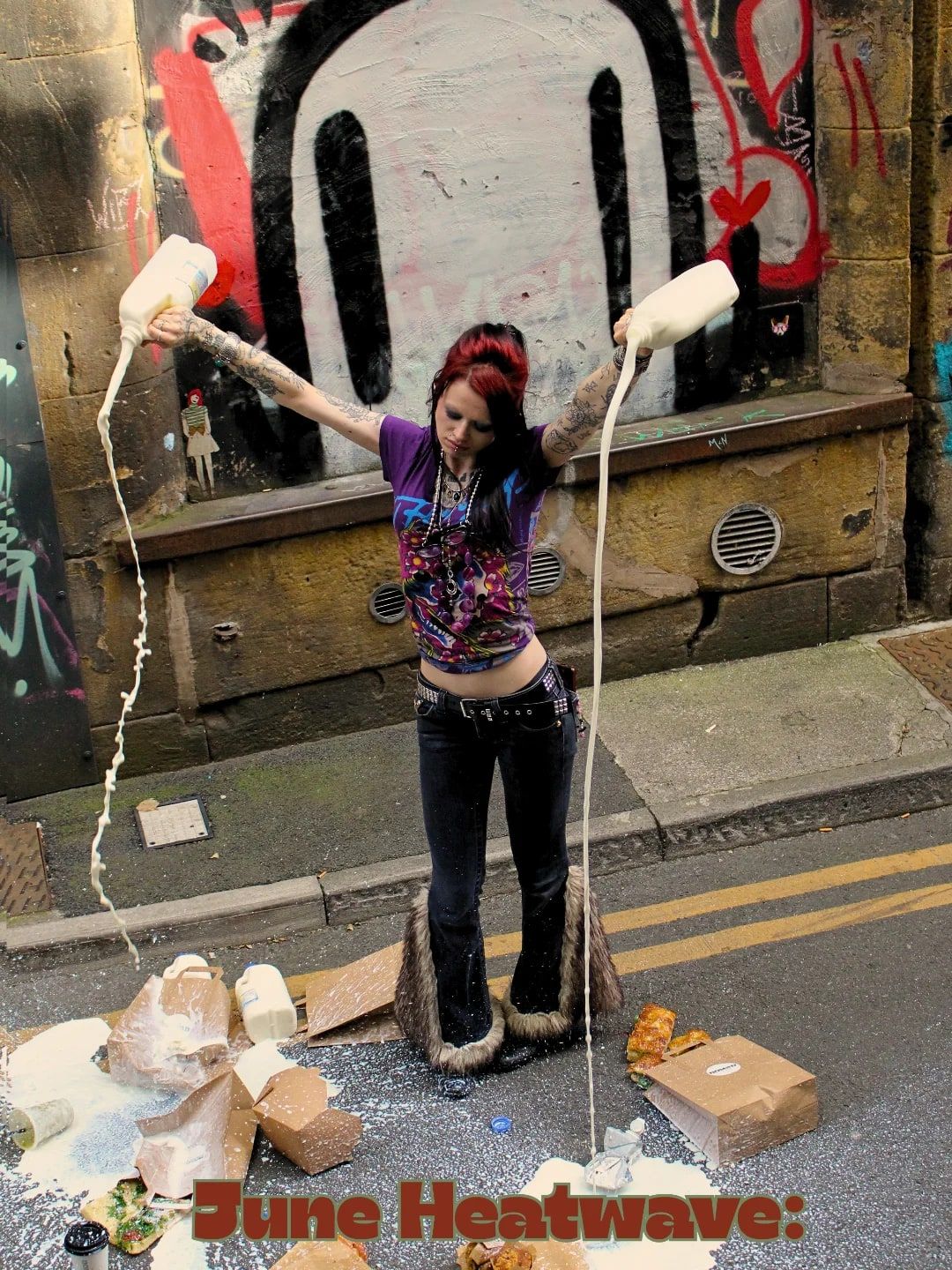 Milk poured everywhere in a graffiti alley — a model laughing, cartons overhead, with “June Heatwave:” in red