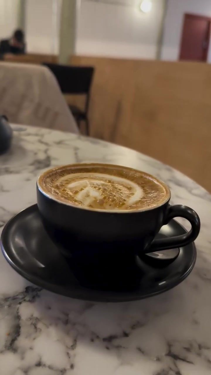 A latte with latte art in a black cup on a marble table