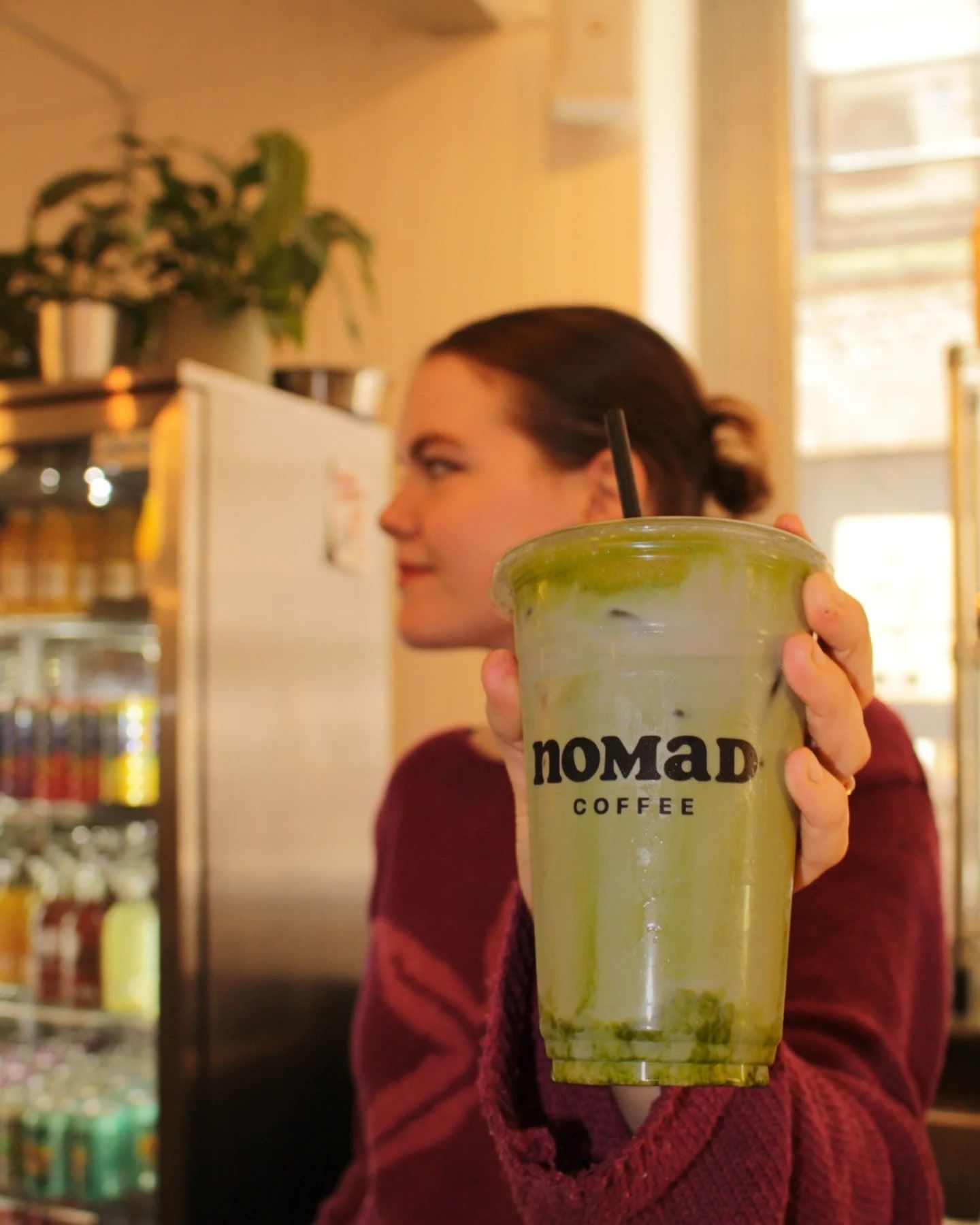 A matcha latte held up to the camera in the warm light of the café