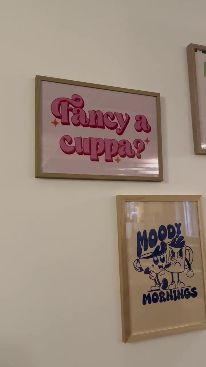 Framed prints on a white wall: “Fancy a cuppa?” in pink and “Moody Mornings” in blue